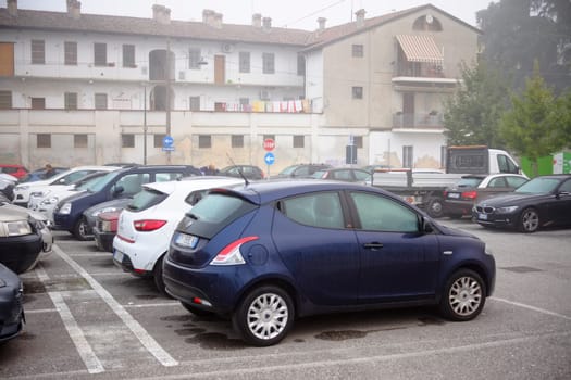 Cremona, Lombardy, Italy - November 7th 2024 Cars parked in parking lot in front of residential building on a foggy day