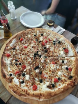Deliciously crafted large pizza is presented on a wooden board, featuring toppings of olives, fresh tomatoes, and melted cheese, perfect for sharing.
