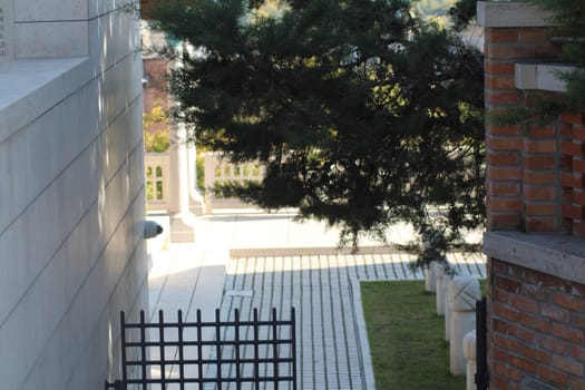 A narrow walkway is bordered by stone walls and lush plants, inviting visitors to explore a serene garden, bathed in sunlight and tranquility.