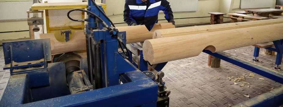 A person operates a wood lathe, shaping logs into wooden pieces in a bright carpentry workshop with various tools around.