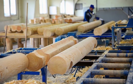 A craftsman meticulously shapes wooden logs using machinery in a well-lit carpentry workshop filled with shavings.