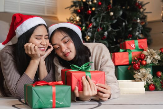Two young women delight in exchanging surprise gifts on Christmas, surrounded by festive decorations and a beautifully lit tree.