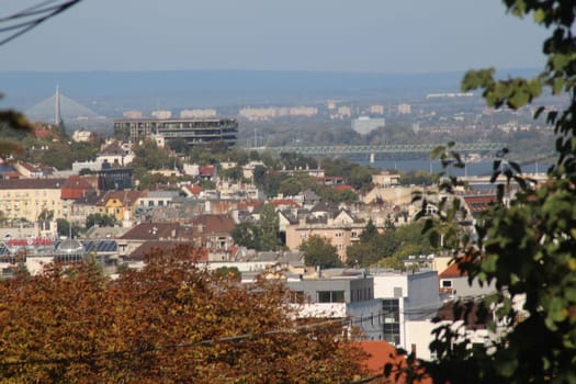 A vibrant town filled with historic buildings and greenery captures the essence of late afternoon. The river and distant hills create a scenic backdrop.