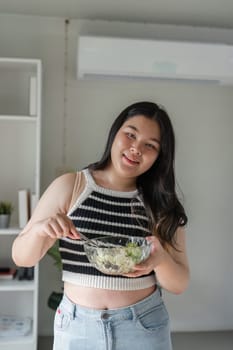 A woman embraces a healthy lifestyle, smiling while preparing a fresh salad in a contemporary home setting.