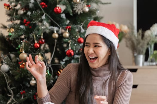 A young woman decorates her room for Christmas, adding festive ornaments to a Christmas tree, creating a warm and joyful holiday atmosphere.