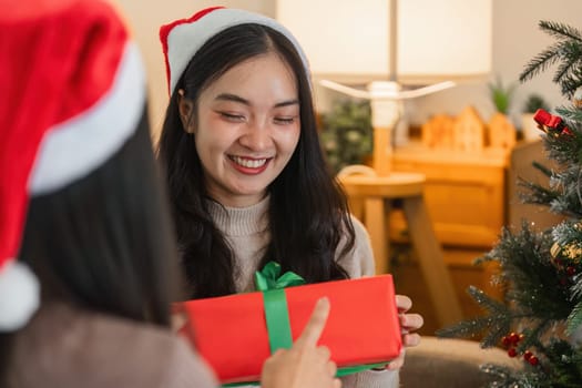 A happy young woman couple exchanging a surprise gift on Christmas day, capturing the joy and warmth of the holiday season.