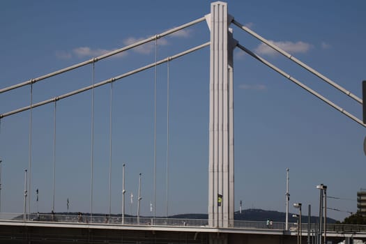 The towering structure of a cable-stayed bridge is prominently displayed against a vivid blue sky, showcasing its modern design. Sunlight highlights the bridge's clean lines.