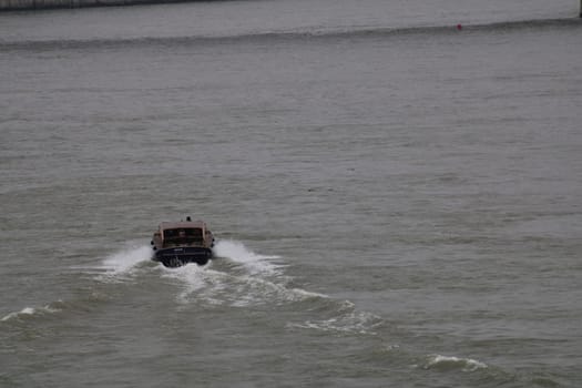 A small boat travels quickly over the water, leaving a wake behind as it navigates through a harbor on a cloudy morning, surrounded by gentle waves.
