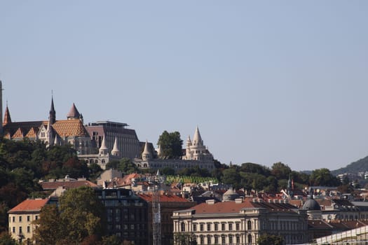 A stunning view of Budapest's historic buildings perched on a hill, showcasing intricate architecture against a clear blue sky, highlighting iconic rooftops.