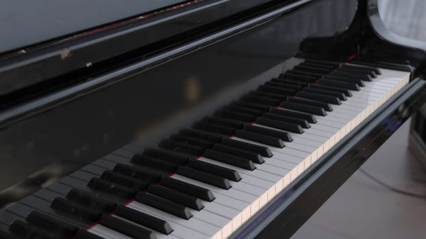 A closeup view of a grand piano beautifully showcasing its sleek black keys and its elegantly polished surface. Clip