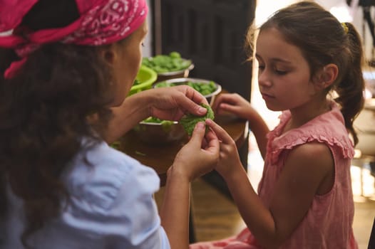 A mother and her young daughter share a moment while preparing fresh vegetables together. The scene exudes warmth, love, and family bonding, highlighting a tender teaching moment.