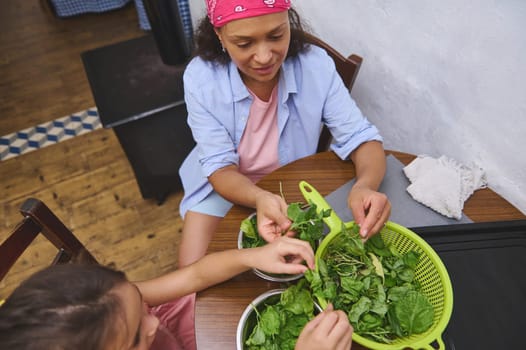 Mother and daughter share a bonding moment as they wash and prepare fresh greens in a cozy kitchen setting, promoting family connection and healthy eating.