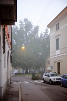 Cremona, Lombardy, Italy - November 7th 2024 Foggy morning in small italian town with street light illuminating big tree