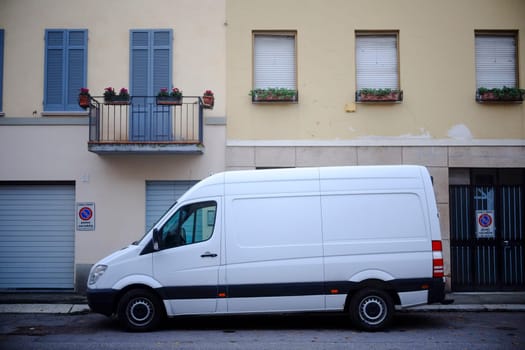 Cremona, Lombardy, Italy - November 7th 2024 White van parked near a residential building with flower boxes and a balcony, representing urban delivery and logistics