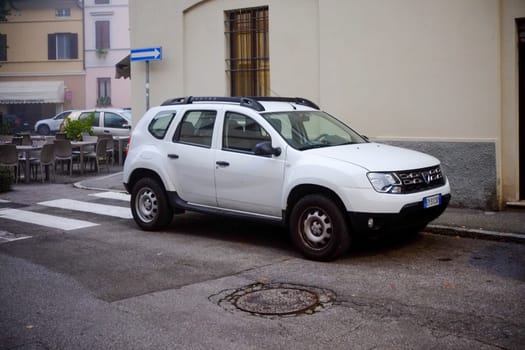 Cremona, Lombardy, Italy - November 7th 2024 White dacia duster parked near a crosswalk and outdoor restaurant tables