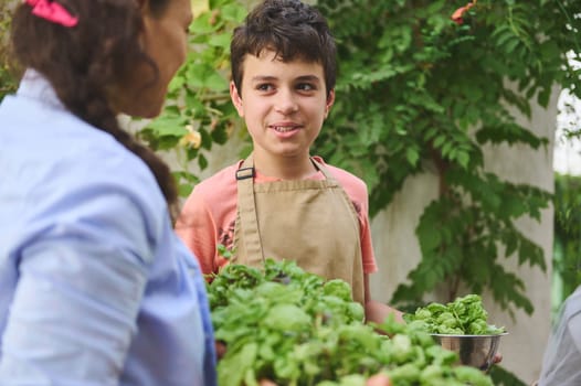 A cheerful child in an apron holds fresh basil leaves while gardening with a family member. The scene is filled with greenery, symbolizing teamwork and a love for nature and gardening.