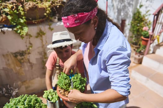 A mother and child are gardening together outdoors. They are nurturing plants, showcasing teamwork and bonding. The setting is bright and sunny, reflecting a peaceful and joyful activity.