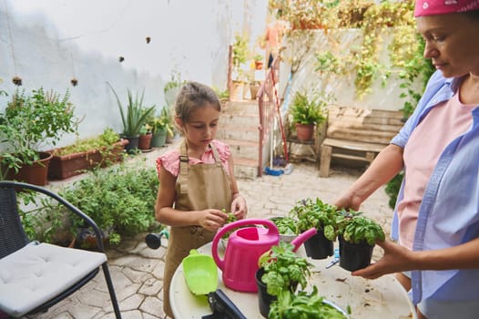 A mother and daughter engage in a gardening activity in their backyard. The child, wearing an apron, learns while planting in pots, surrounded by greenery in a warm and sunny setting.