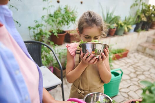 A young girl in an apron smells fresh vegetables in a garden setting. The scene conveys joy and a connection with nature, reminding us of the simple pleasures of homegrown produce.