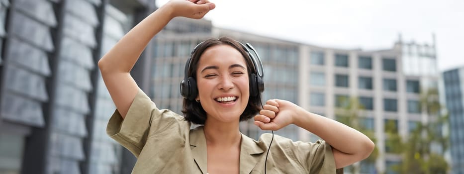 Girl dances on street with headphones on, listens to music and feels happy walking in city.