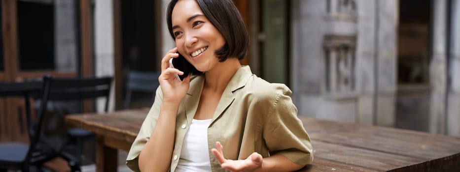 Young woman having conversation on mobile phone, sitting outdoors and making phone call, using smartphone, talking.