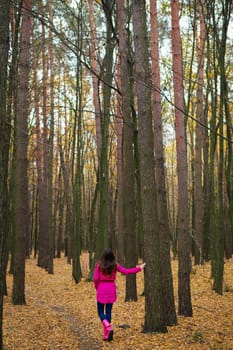 girl in a raincoat and pink rubber boots walking in an autumn forest.