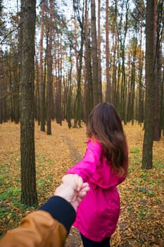 girl in a pink raincoat holds her boyfriend's hand in the autumn forest.