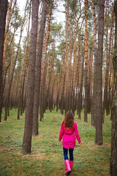 girl in a raincoat and rubber boots walking alone in the woods.