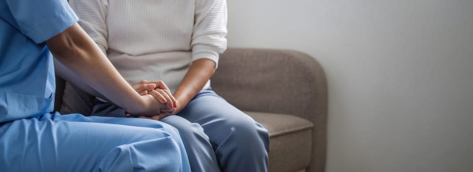 Happy patient is holding caregiver for a hand while spending time together. Elderly woman in nursing home and nurse.