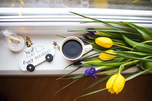 beautiful flowers-tulips and irises lie on the windowsill with a typewriter, a Christmas tree, a cup of coffee.