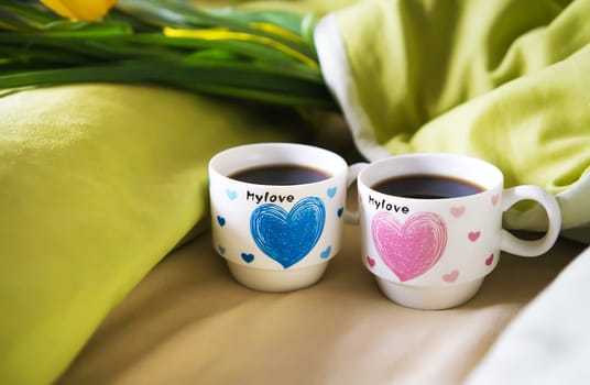 two cups of coffee stand on the bed with a bouquet of flowers, close-up.