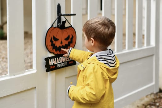 A boy with Carved pumpkin on the fence of the house