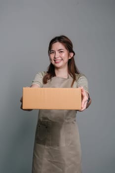 Young asian woman startup small business freelance holding parcel box standing isolated on grey background, Online marketing packing box delivery concept.