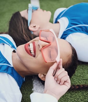 Friends, sports and laying on field, break and closeup of sunglasses, smile and relax for practice, training and workout. Happy people, playful and lazy for exercise, fashion and accessories for fun.