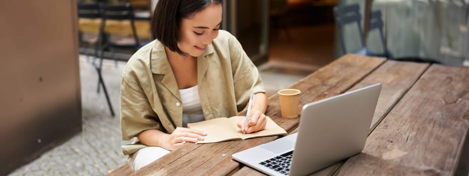 Portrait of young asian woman working on laptop, making notes, writing down while attending online lesson, work meeting.