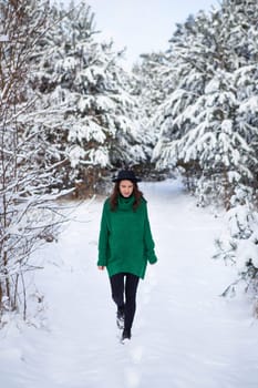 A young girl in a dark green sweater and hat stands in the middle of a beautiful winter forest