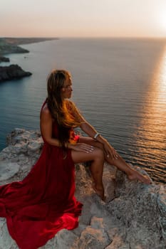 Woman sunset sea red dress, side view a happy beautiful sensual woman in a red long dress posing on a rock high above the sea on sunset