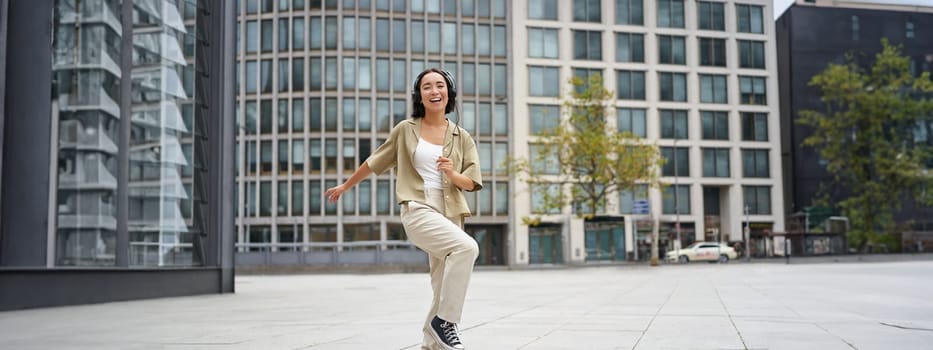 Happy people in city. Upbeat young girl dancing on street in headphones, listening music in headphones.