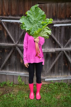A woman in pink boots and a pink sweater holds a bouquet of rhubarb in her hands