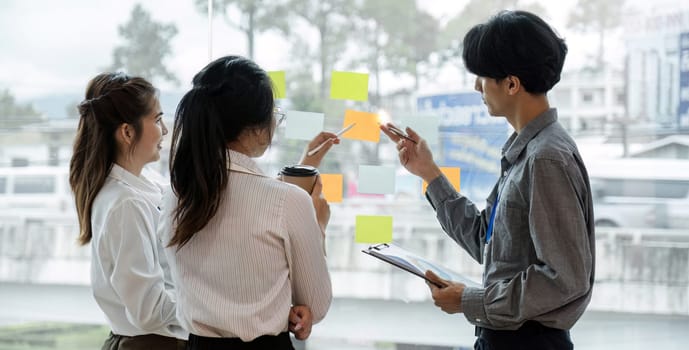 team employees busy brainstorming develop business ideas write on colorful sticky notes, concentrated colleagues share thoughts on pads on glass window.