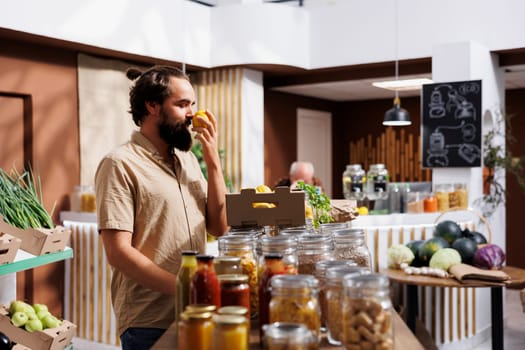 Green living man enjoying the fresh smell of locally grown lemons in zero waste supermarket. Customer happy to find eco friendly organic fruits in local neighborhood store