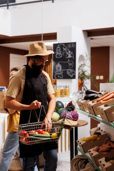 Hipster in zero waste supermarket filling shopping basket with healthy locally grown vegetables. Environmentally conscious customer buying organic non GMO food from local neighborhood shop