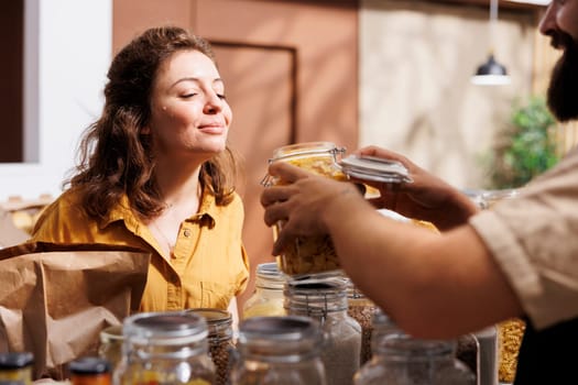 Storekeeper showing woman shopping in zero waste grocery store organic healthy bulk products in reusable packaging. Vendor in local neighborhood shop recommending food item to customer