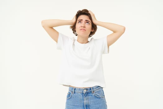 Portrait of woman in panic, grabs her head, feeling troubled, has big problem, stands anxious against white backgrond.