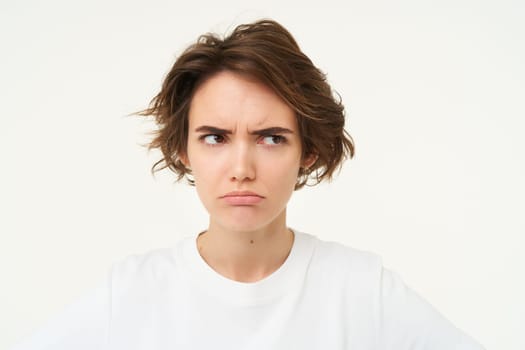 Close up of brunette woman shows angry face, frowning grumpy, pouting and looking disappointed, standing over white background. Copy space