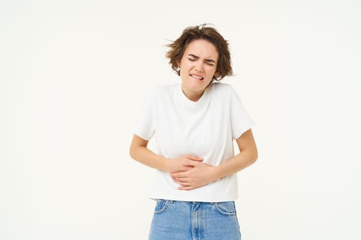 Image of woman with stomach ache, touching her belly, grimacing from pain or discomfort, has painful menstrual cramps, isolated over white background.
