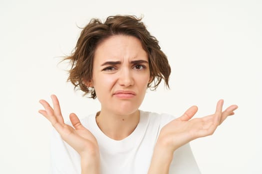 Close up of shocked brunette woman, shrugging and looking disappointed, posing over white studio background.