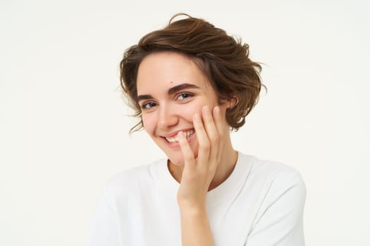 Portrait of brunette woman laughing, smiling and covering face with hand, looking shy and cute, standing over white background. Copy space