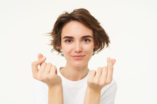 Close up of brunette woman shows finger hearts gesture and smiles, isolated over white background.
