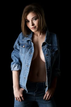 Pretty sexy girl in unbuttoned jeans jacket shot against black wall